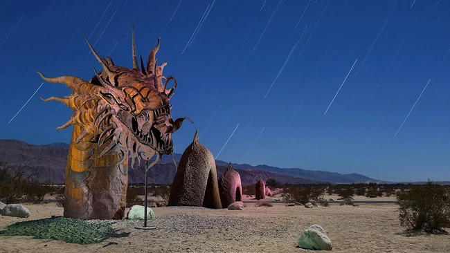 Large wooden dragon sculpture with elaborate carved details stands in a desert landscape under a starry night sky.