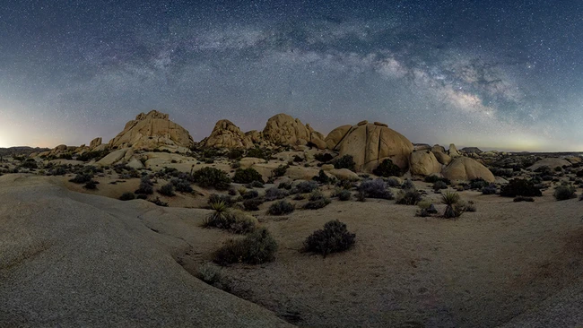 Desert landscape with large granite rock formations under a starry night sky with visible Milky Way.