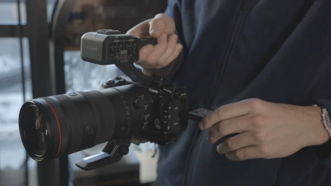 Videographer operating professional cinema camera with attached monitor and telephoto lens