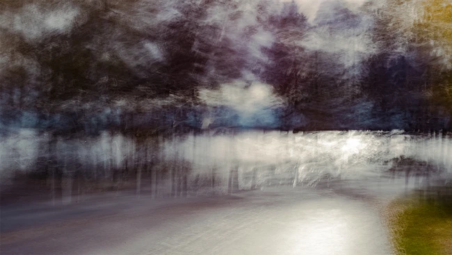 Soft-focus landscape with frozen lake, dark forest treeline, and moody winter sky