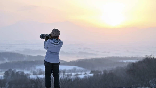 Photographer shooting landscape from snowy hilltop at sunrise