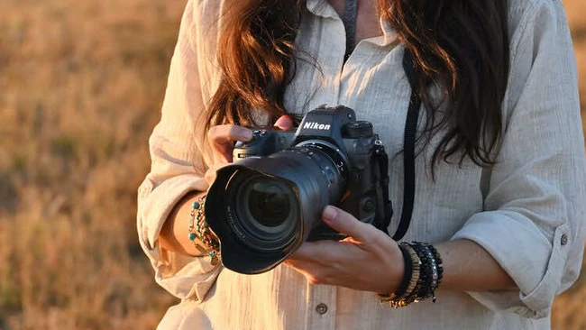 Photographer holding a DSLR camera with telephoto lens during golden hour outdoors.