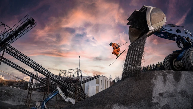 Skier launching airborne from industrial landscape at golden hour