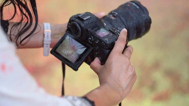 Photographer holding a DSLR camera with a telephoto lens in muddy conditions outdoors