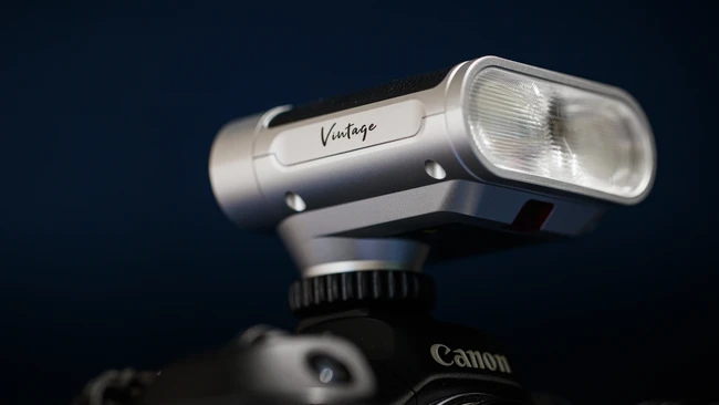 Vintage camera flash mounted on Canon DSLR against dark blue background