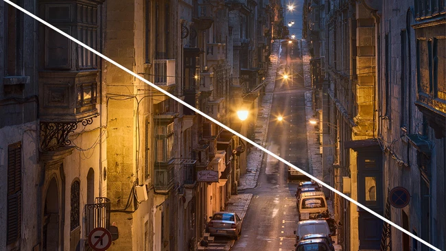 Narrow European street at dusk split diagonally into warm and cool lighting zones