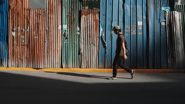 Person walking past corrugated metal walls with bold blue, rust, and green coloring