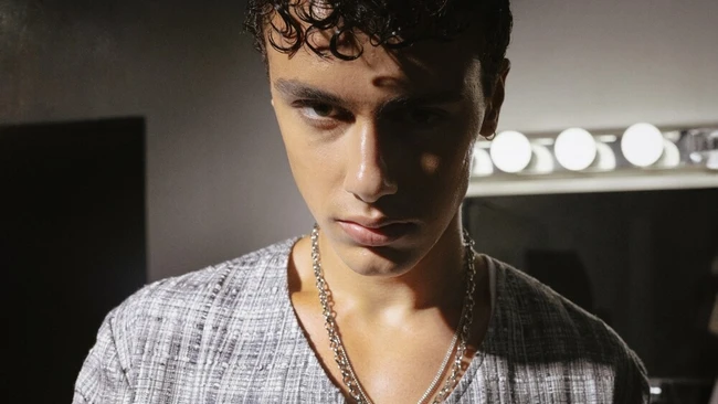 Portrait of young man with curly dark hair wearing gray shirt and chain necklace