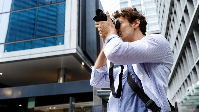 Photographer in light blue shirt holding camera up to compose shot in urban downtown setting