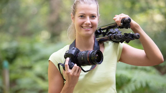 Young woman holding professional binoculars outdoors with green foliage background