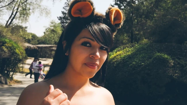Woman with orange bear ear headband smiling at camera in sunlit outdoor garden setting