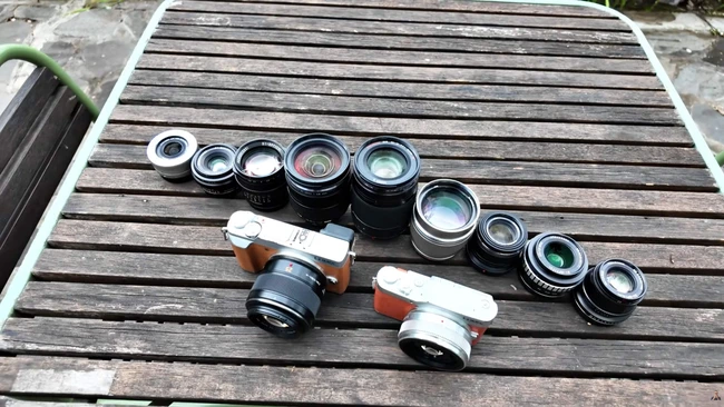 Collection of vintage rangefinder camera lenses and two film camera bodies arranged on wooden surface