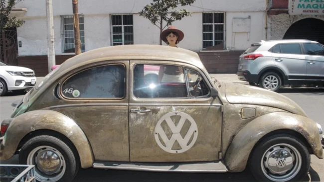 Vintage Volkswagen Beetle with patina finish and VW logo, driver visible through open window
