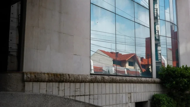 Reflective glass facade mirrors residential buildings with red roofs against concrete brutalist architecture
