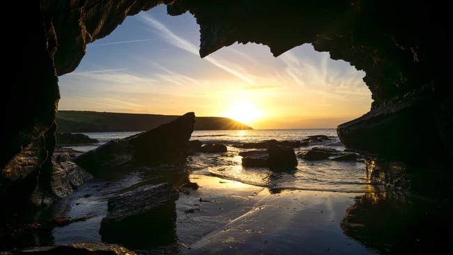 Golden sunset framed through a sea cave opening with silhouetted rocks
