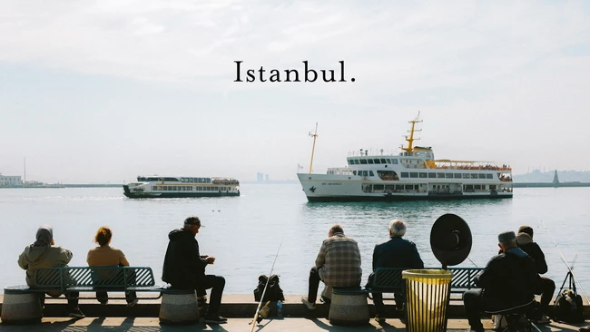 People sitting on a waterfront bench overlooking ferries on the Golden Horn in Istanbul