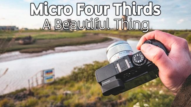 Hand holding Micro Four Thirds camera against riverside landscape backdrop