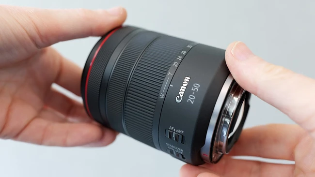 Canon RF 24-50mm lens held in hands against neutral background