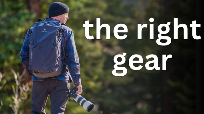 Photographer wearing backpack and beanie while holding telephoto lens in forest setting