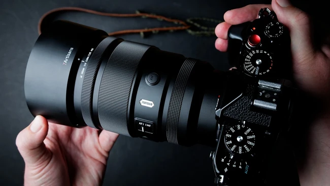 Photographer's hands holding mirrorless camera with telephoto lens against dark background