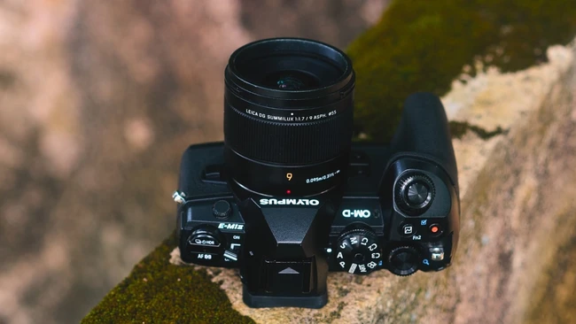 Compact mirrorless camera with attached prime lens mounted on moss-covered stone surface