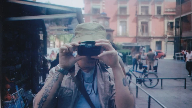 Photographer holding vintage film camera up to face in urban plaza