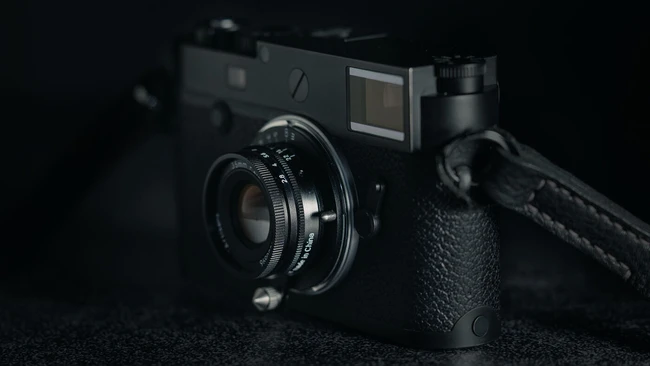 Black rangefinder camera with attached lens and shoulder strap on dark textured surface