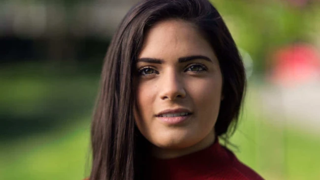 Portrait of a woman with long dark hair wearing a burgundy turtleneck against a blurred green background