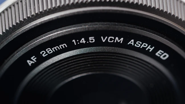 Close-up of AF 28mm 1:4.5 VCM ASPH ED camera lens barrel against blue sky