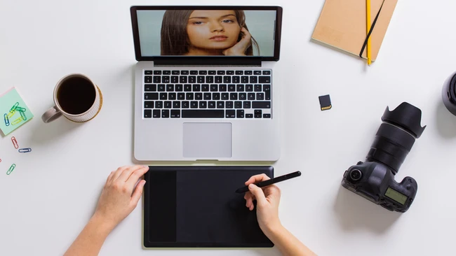 Photographer's overhead desk setup with laptop, graphics tablet, camera, and coffee