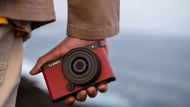 Person holding red Lumix compact camera with ocean backdrop