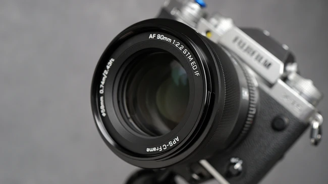 Fujifilm camera with AF 90mm f/2.4 R LM OIS lens mounted, shot against neutral gray background