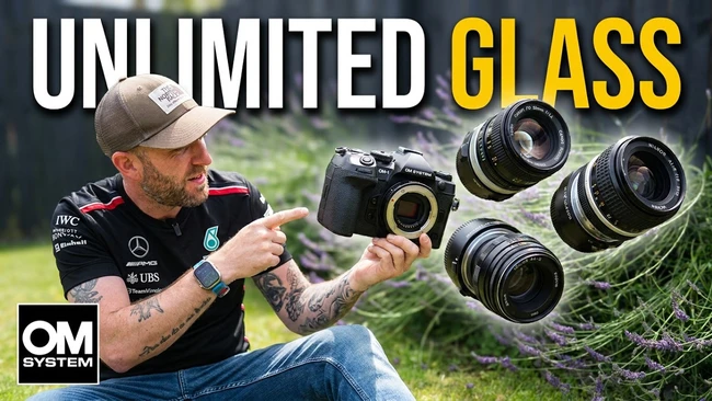 Photographer holding OM System camera with multiple lenses displayed outdoors