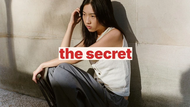 Woman sitting against concrete wall with text overlay reading 'the secret'