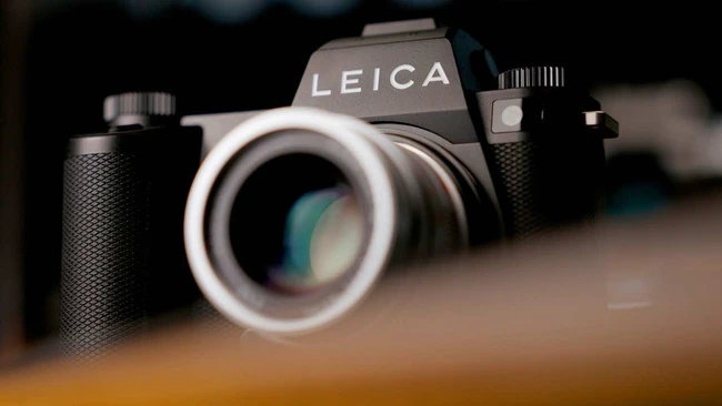 Leica SLR camera with telephoto lens on wooden surface, shallow depth of field
