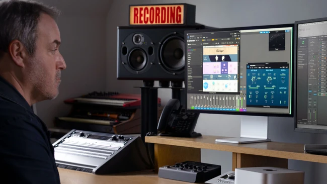 Audio engineer at professional recording studio workstation with dual monitors and studio speakers