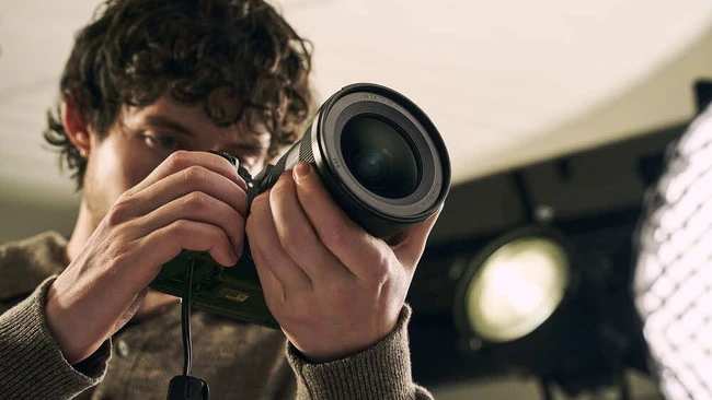 Photographer holding camera up to eye with both hands, shot from front with warm golden hour lighting