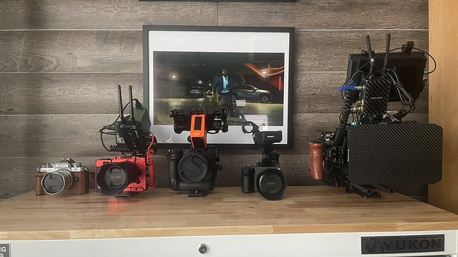 Filmmaker's workspace displaying cameras, lenses, and production gear on wooden desk