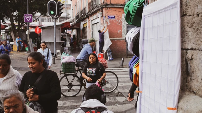 Busy urban street scene with pedestrians and a cyclist among market stalls and storefronts