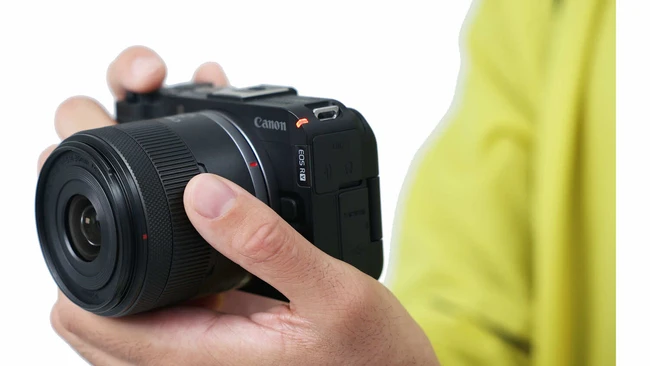 Hand holding a compact mirrorless camera with black body and lens