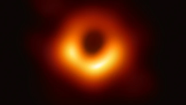 First photograph of a black hole showing bright orange and yellow accretion disk with dark central shadow