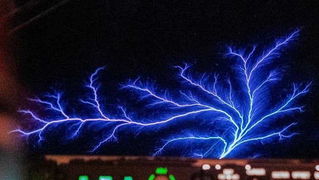 Electric blue lightning branching across dark sky with warm city lights below