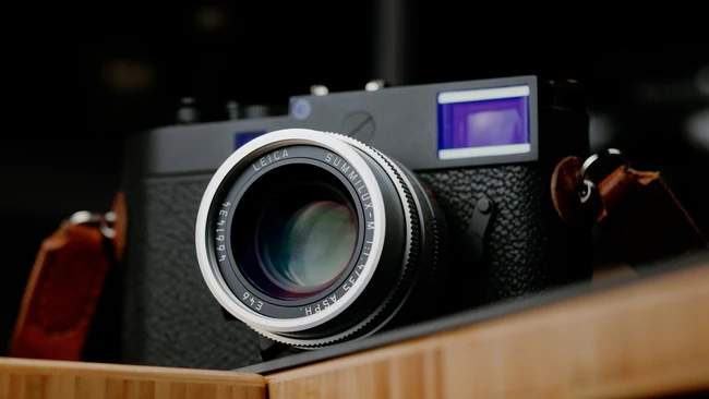 Rangefinder camera with chrome lens and textured black body displayed on wooden surface