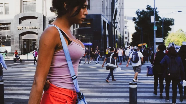Woman in pink tank top and red shorts on urban crosswalk with crowds and city buildings in background
