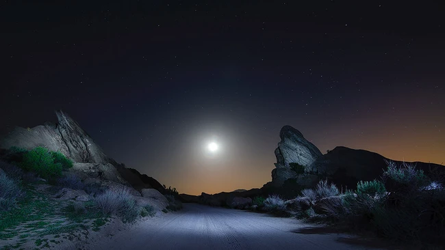 Desert landscape under full moon with illuminated rocky outcrops and sparse vegetation