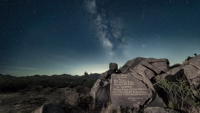 Milky Way galaxy rising above desert landscape with illuminated memorial plaque on boulder