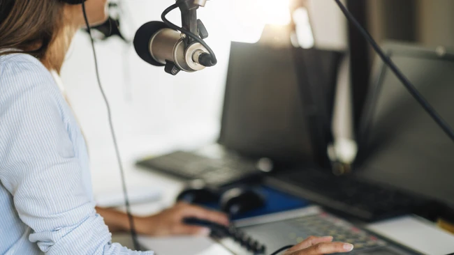 Podcaster recording into a large-diaphragm condenser microphone at a desktop studio setup