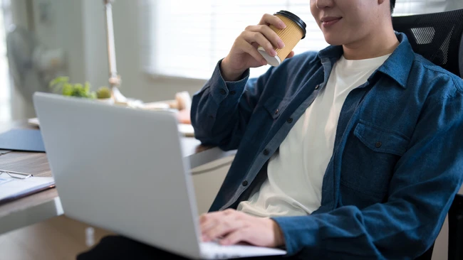 Person holding coffee cup while working on laptop at desk