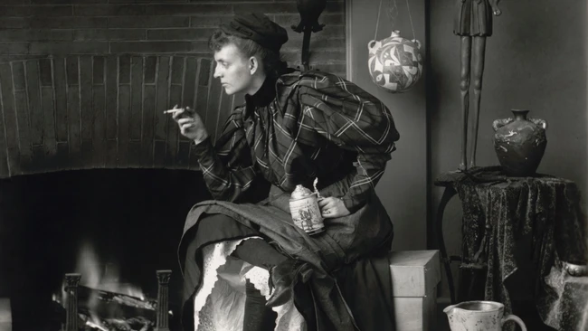 Woman in dark clothing sits by fireplace in vintage interior setting