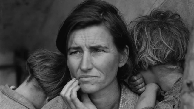Woman with contemplative expression holding two young children close to her shoulders